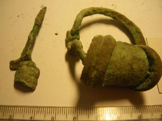 Jonuks 2) Uugla III kivikalme: AI 1068: 175 176 Fassetitud otstega hoburaudsõlg: kuusnurkse läbilõikega kaar, kaunistusteta, d= 3 3,5 cm, sõlenõel murdunud, nõela kannal kuuseoksa motiiv, lai